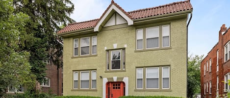 A two-story building with a red door, multiple windows, and a brick facade.