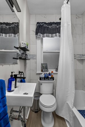 Et badeværelse med hvid vask, toilet og badekar. Der er håndklæder og toiletartikler på vasken.