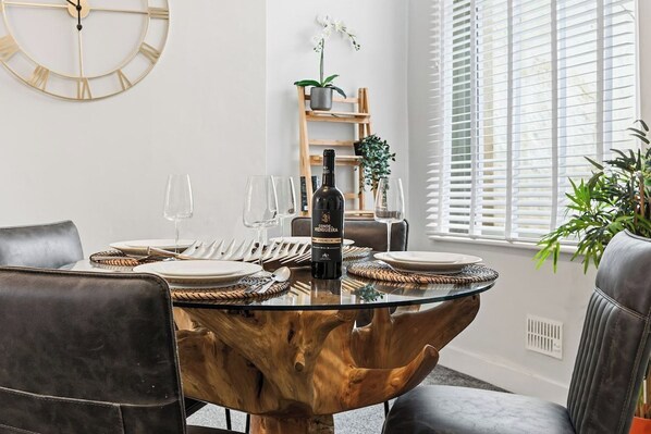 A dining area with a round glass table, leather chairs, and a bottle of wine.