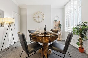 Un comedor con una mesa redonda, sillas negras, un reloj de pared y una planta en maceta.