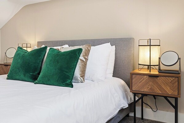 A neatly made bed with white bedding and two green pillows, flanked by two bedside tables with lamps.