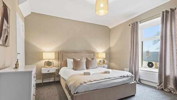 A bedroom with a large bed, bedside lamps, a nightstand, a dresser, and a window with curtains. - Stunning 3B Home, ideal for leisure & contractors (Clitheroe)