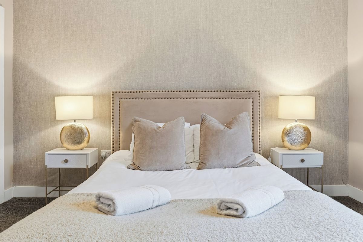 A neatly made bed with two pillows, a white headboard, and two bedside lamps with decorative bases.