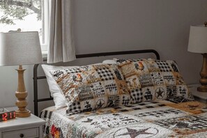 A bed with a quilt featuring various patterns and text, flanked by two bedside lamps and a digital clock. - Mount Vernon IL Large Family Farmhouse with Game Room, Silo Gazebo, & Pond (Mount Vernon)