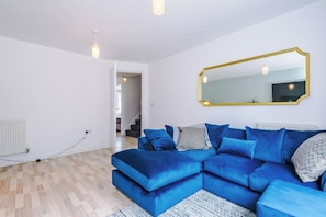 A modern living room with a sectional sofa, a large mirror, and a staircase leading to another level. - Spacious 6 bedroom house, with private parking (Manchester, London)
