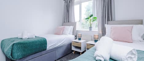A twin room with two beds, a window with curtains, bedside tables with lamps, and a potted plant.