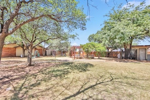 A fenced outdoor area with picnic tables, a brick building, and trees. - Peaceful Lubbock Retreat with Private Indoor Atrium (Lubbock)