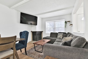 A living room with a flat-screen TV mounted on the wall, a fireplace, a sofa, a coffee table, and a dining table with chairs. - Peaceful Lubbock Retreat with Private Indoor Atrium (Lubbock)