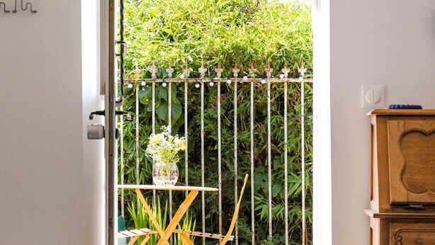 Une pièce avec un meuble en bois, une table blanche et une vue sur un jardin par une porte ouverte.