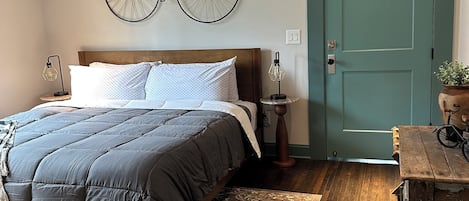 Une chambre à coucher avec un lit, une décoration murale représentant un vélo, une porte et une table de chevet avec une lampe.