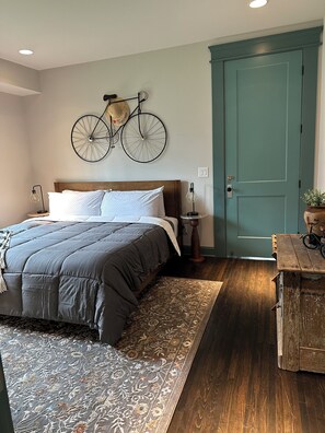 A bedroom with a bed, a bicycle wall decoration, a door, and a nightstand with a lamp. - The Fox Den in delightful Columbia (Columbia)