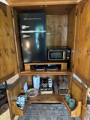 Eine kompakte Küche mit einem schwarzen Kühlschrank, einer Mikrowelle und einer kleinen Kaffeemaschine.