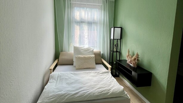 A bedroom with a bed, a nightstand, a lamp, and a window with curtains.