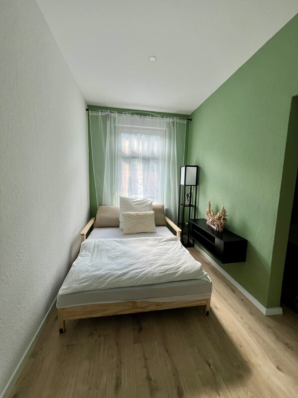 A bedroom with a bed, a nightstand, a lamp, and a window with curtains.