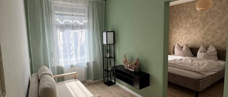 A room with a sofa, a small table, a bed, and a wall-mounted shelf.