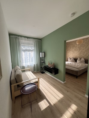 Una habitación con sofá, una mesita, cama y estante en la pared.