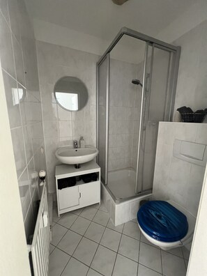 Un baño con un lavamanos blanco, un espejo, cabina de ducha y un inodoro.