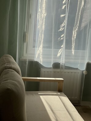 A room with a window covered by sheer curtains, a radiator, and a sofa.
