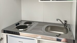 A compact kitchenette with a microwave, stove, sink, and storage cabinets.
