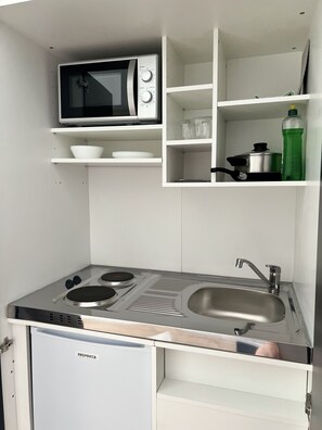 Una kitchenette compacta con microondas, estufa, fregadero y armarios de almacenamiento.