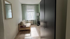 A room with a large wardrobe, a sofa, a small table, and a window with curtains.