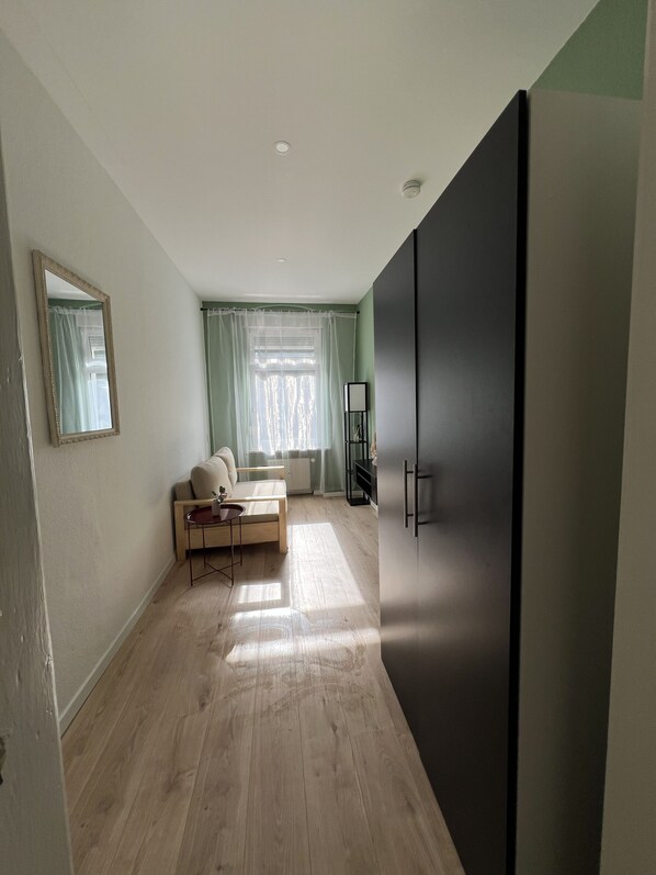A room with a large wardrobe, a sofa, a small table, and a window with curtains.