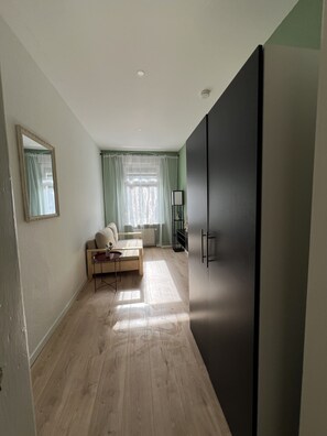 Una habitación con un armario grande, un sofá, una mesita y una ventana con cortinas.