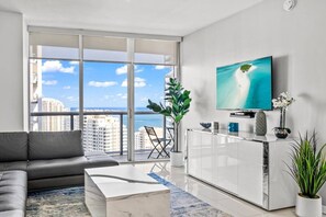A modern living room with a sofa, coffee table, and a TV on a wall. - High-Floor 1BR | Bay & City Views | Brickell (Miami)