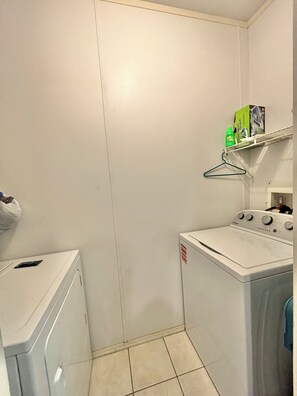 Een wasserette met een wasmachine, droger en een plank met een doos en een fles.