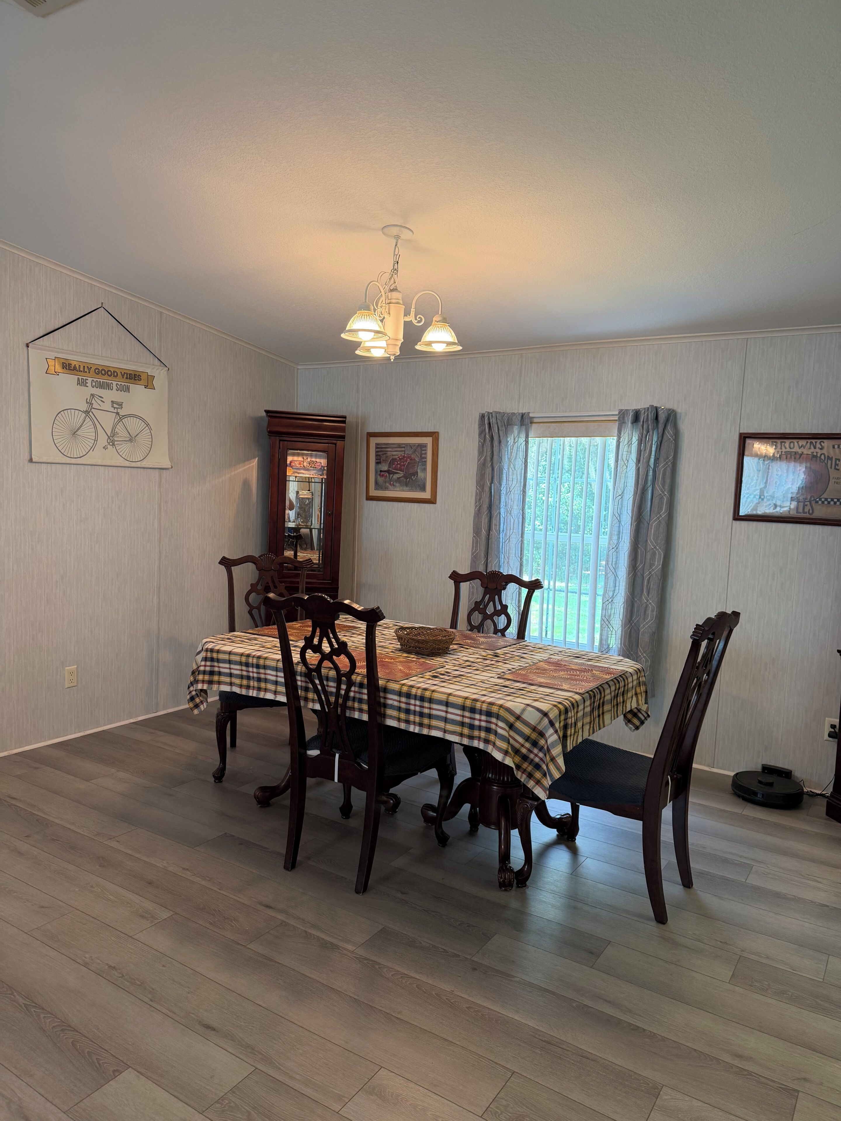 A dining area with a table set for four, wooden chairs, a chandelier, and a window with curtains.