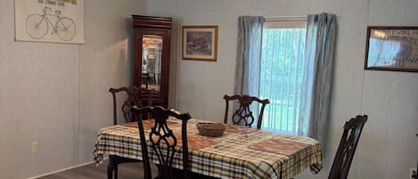 A dining area with a table set for four, wooden chairs, a chandelier, and a window with curtains.