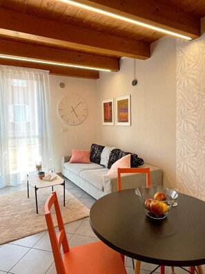 A cozy living room with a sofa, a round table with fruit, and a clock on the wall.
