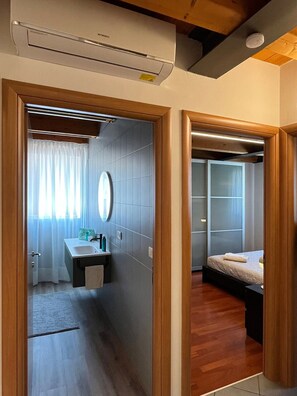 A hotel room with a wooden floor, a bed, a bedside table, a mirror, and a window with curtains.