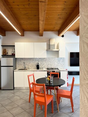 A modern kitchen with white cabinets, a granite countertop, and a round table with orange chairs.