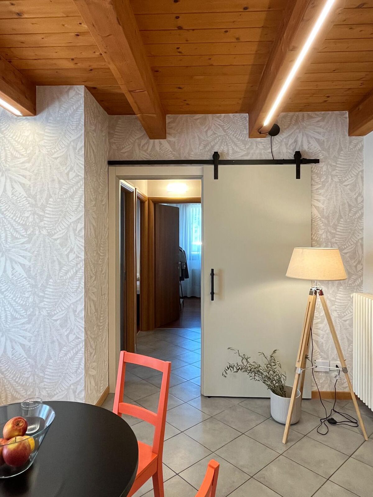 Une pièce avec un plafond en bois, une porte coulissante, une table avec des fruits, une lampe et une plante en pot.