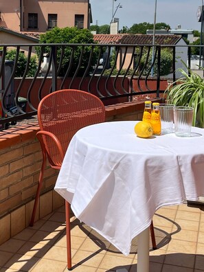 A table set outdoors with a white tablecloth, a wicker chair, and a bottle of water.