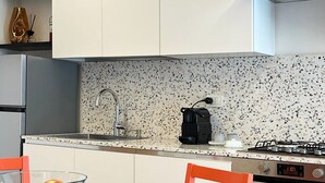 Una cocina moderna con armarios blancos, salpicadero con motas y una estufa a gas, además de una cafetera.