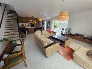 A modern living room with a sofa, a coffee table, and a dining area with a kitchen in the background. - A 4-bedroom family home located between Bayonne, Biarritz, and the Landes region. (TARNOS)