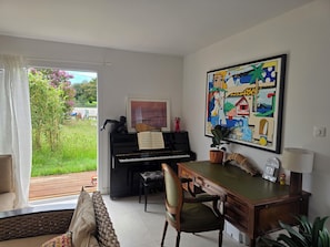 A room with a piano, a desk, a chair, a large abstract painting, and a view of a garden through a glass door. - A 4-bedroom family home located between Bayonne, Biarritz, and the Landes region. (TARNOS)