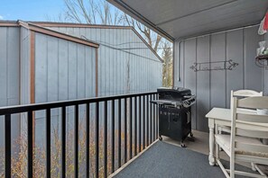 Ein überdachter Balkon mit Grill, einem weißen Stuhl und einem kleinen Tisch.