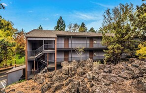 A multi-story building with balconies, a staircase, and a rocky landscape. - Top Floor Downtown Condo With Balcony & Grill! (Bend)