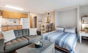 Een knus woongedeelte met een bank, een bed, een eettafeltje en een kitchenette.