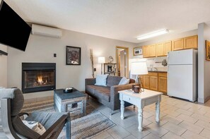 A living room with a fireplace, a sofa, a coffee table, and a television. - Top Floor Downtown Condo With Balcony & Grill! (Bend)