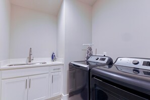 A compact kitchen with a sink, a small countertop, and a washing machine. - Luxury East Nashville Dual Townhomes | Walk to Five Points | 8 Bedrooms |2 Arcade Lounges (Nashville)