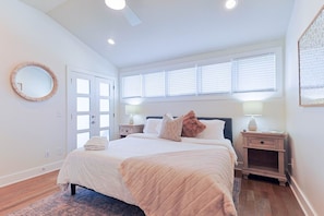A bedroom with a large bed, bedside tables, a round mirror, and a window with blinds. - Luxury East Nashville Dual Townhomes | Walk to Five Points | 8 Bedrooms |2 Arcade Lounges (Nashville)
