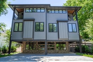 A modern two-story house with a stone foundation, large windows, and a balcony on the upper floor. - Luxury East Nashville Dual Townhomes | Walk to Five Points | 8 Bedrooms |2 Arcade Lounges (Nashville)