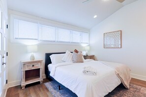 A bedroom with a large bed, two bedside tables, a window with blinds, and a decorative wall piece. - Luxury East Nashville Dual Townhomes | Walk to Five Points | 8 Bedrooms |2 Arcade Lounges (Nashville)