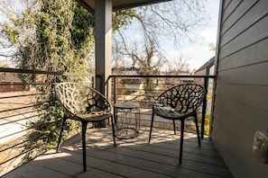 A covered outdoor area with two metal chairs and a small table, surrounded by a wooden deck and metal railing. - Luxury East Nashville Dual Townhomes | Walk to Five Points | 8 Bedrooms |2 Arcade Lounges (Nashville)
