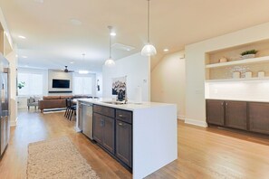 A modern kitchen with a central island, pendant lighting, and a dining area with a sofa and chairs. - Luxury East Nashville Dual Townhomes | Walk to Five Points | 8 Bedrooms |2 Arcade Lounges (Nashville)