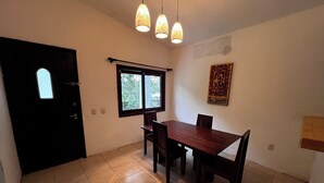 A dining area with a wooden table and chairs, a window with a view, and a door. - House with a spacious yard surrounded by jungle and trees, ideal for families (Xpujil)